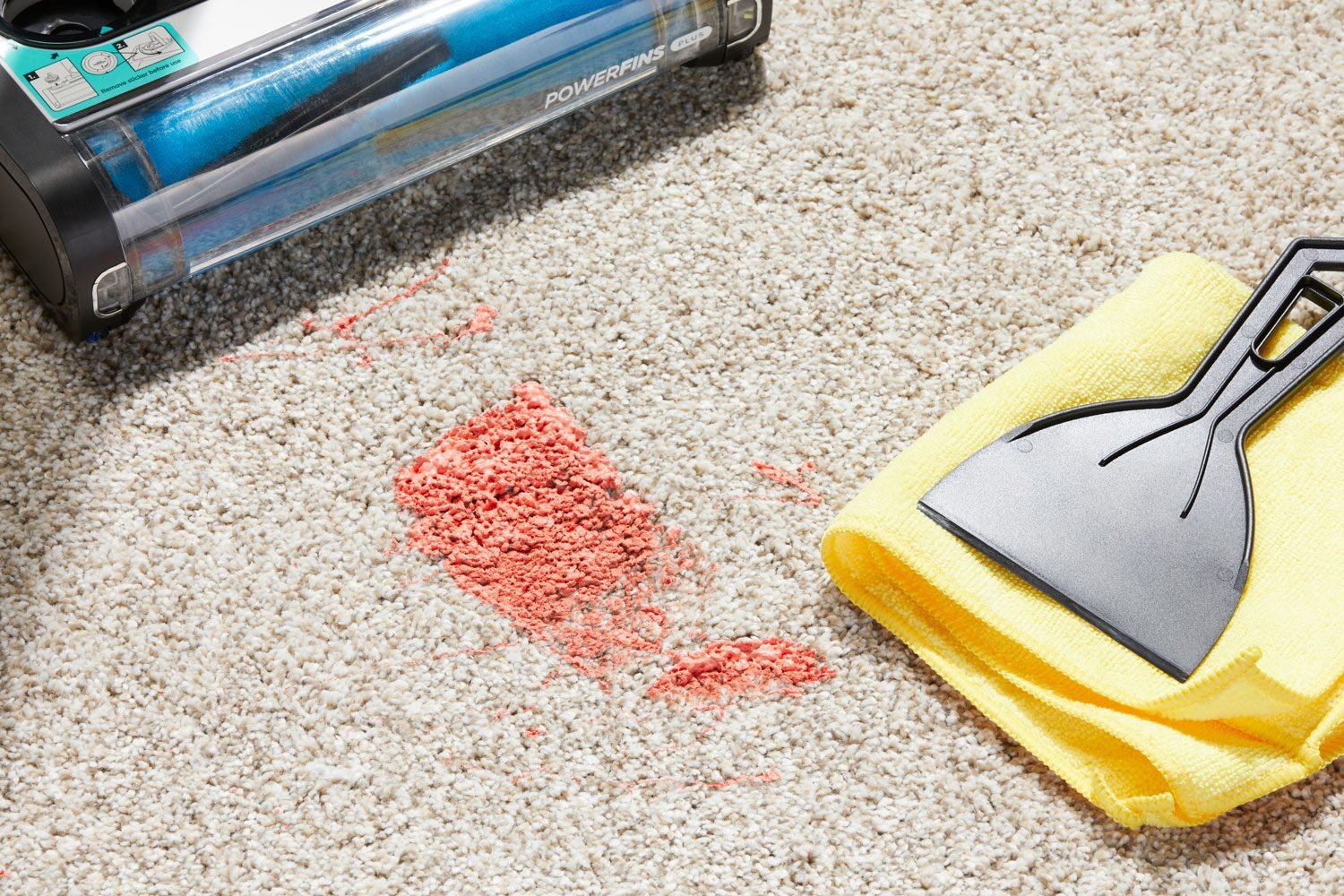 Dried paint stain on a carpet with paint scraper, towel, and vacuum cleaner nearby