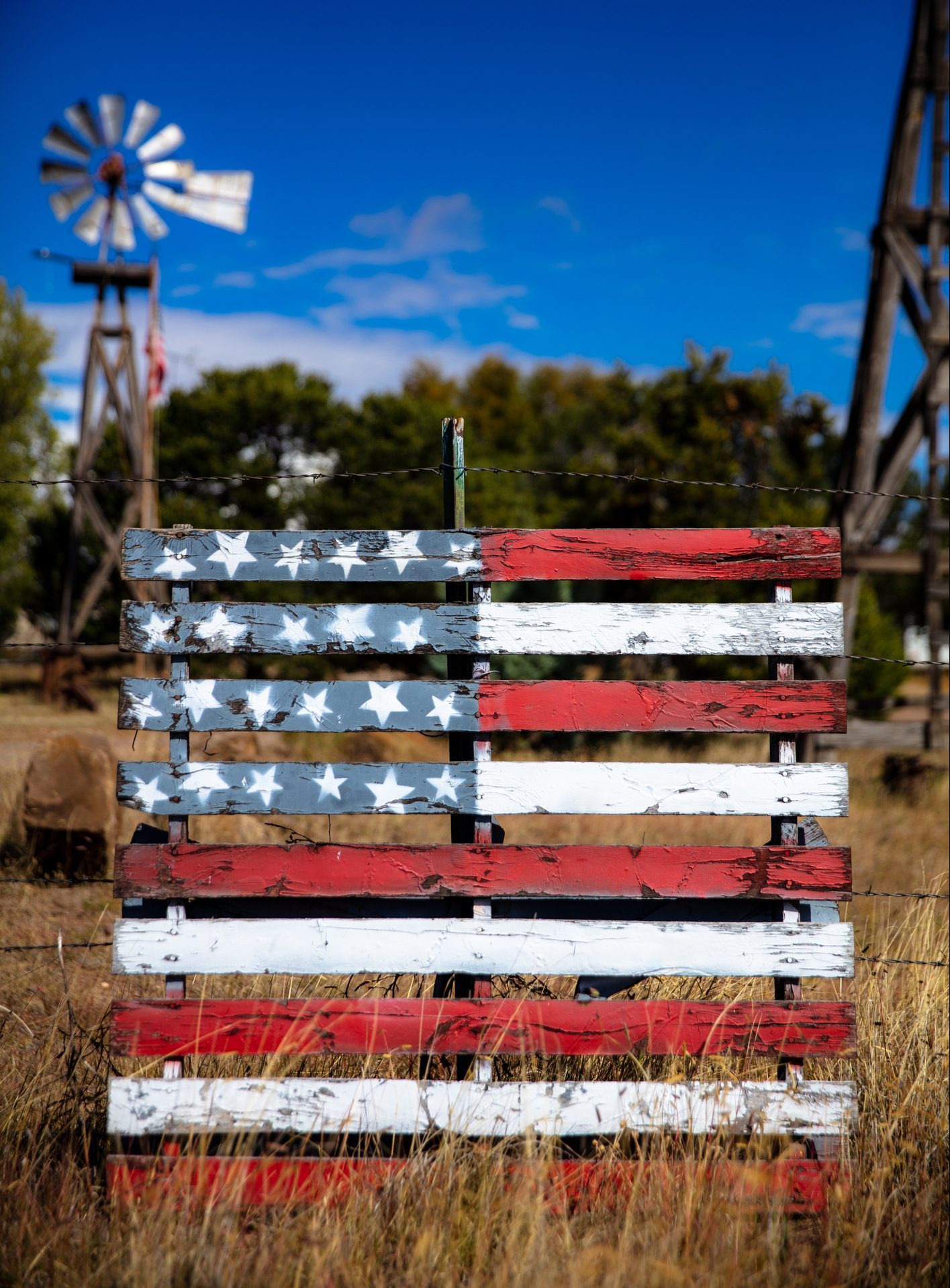 An old fashioned windpump against a bright blue sky behind a wooden pallet painted with the stars and stripes of the american flag