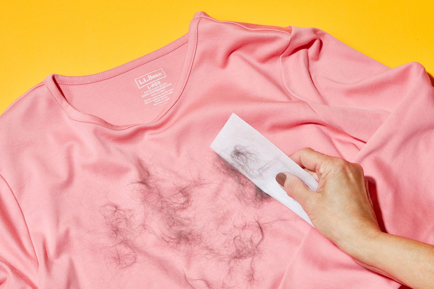 hand using dryer sheet to remove pet hair from a pink shirt on orange background