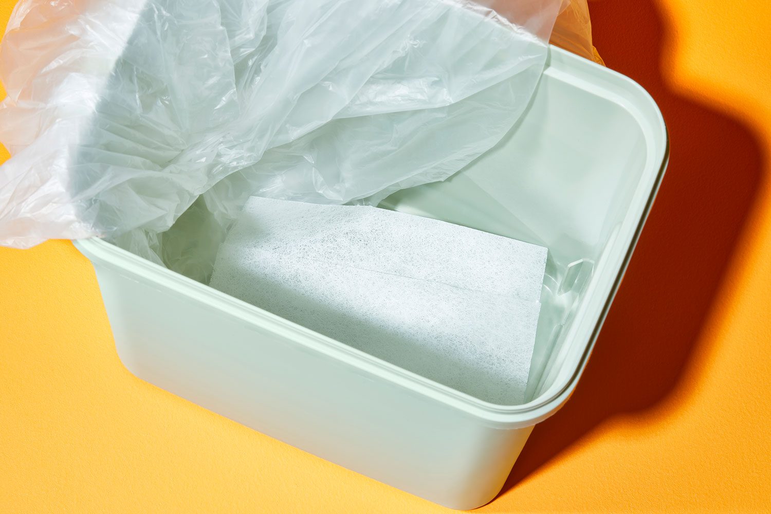 a dryer sheet at the bottom of a trash can with the bag pulled to one side so the dryer sheet can be visible; orange background