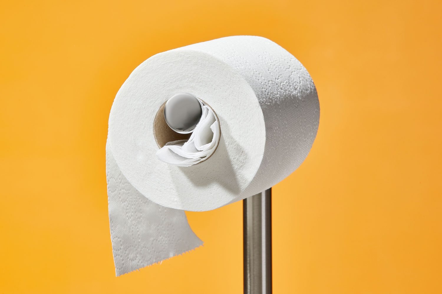 dryer sheet poking out of the cardboard roll of a toilet paper roll; orange background