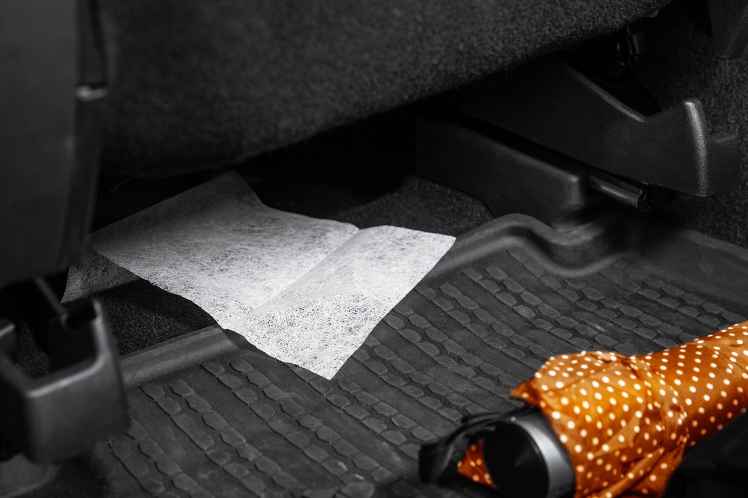 close up of a dryer sheet under a seat of a car; orange umbrella on the car floor nearby
