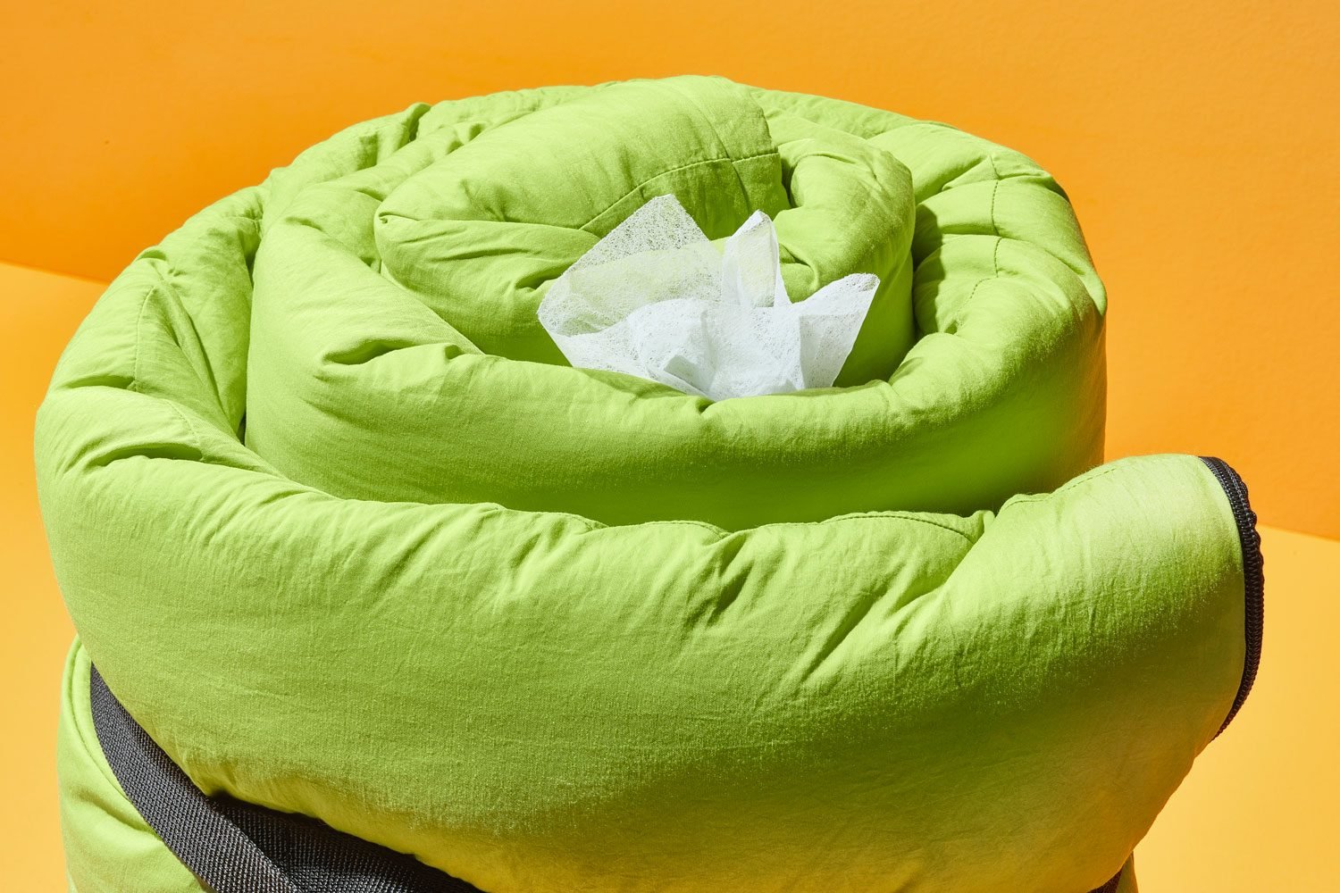 dryer sheet poking out of a rolled up green sleeping bag; orange background