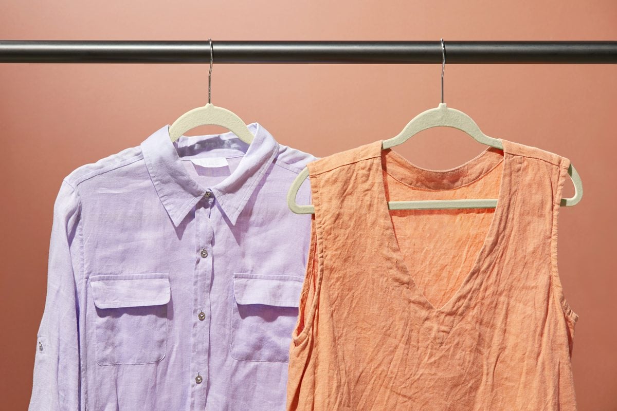 two wrinkled shirts hanging on a garment bar, a lavender button down and an orange sleeveless blouse