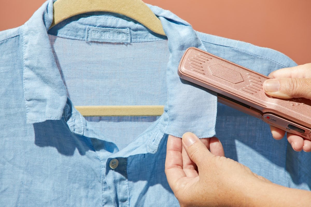 hands using a hair straightener to remove wrinkles from the collar or a blue button down shirt