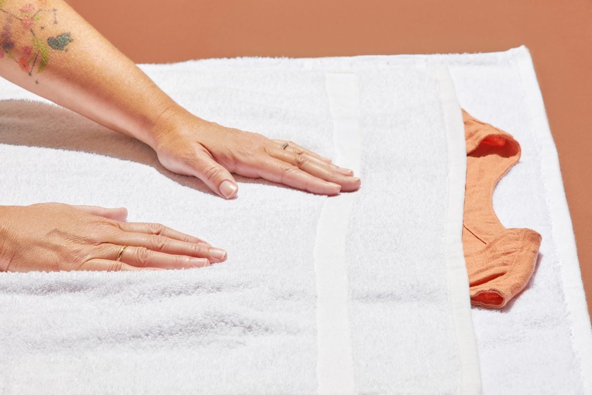 Hands using the damp towel method to remove wrinkles from an orange sleeveless blouse