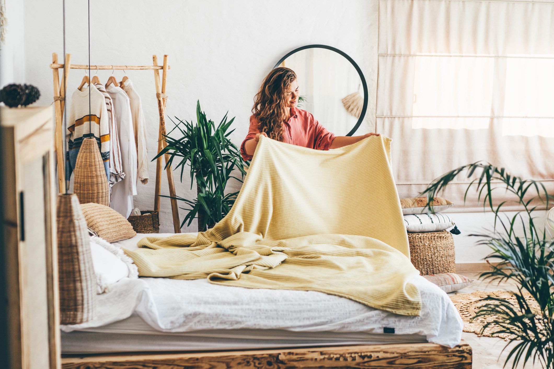 Woman doing her morning routine, arranging pillows and making up bed at home.