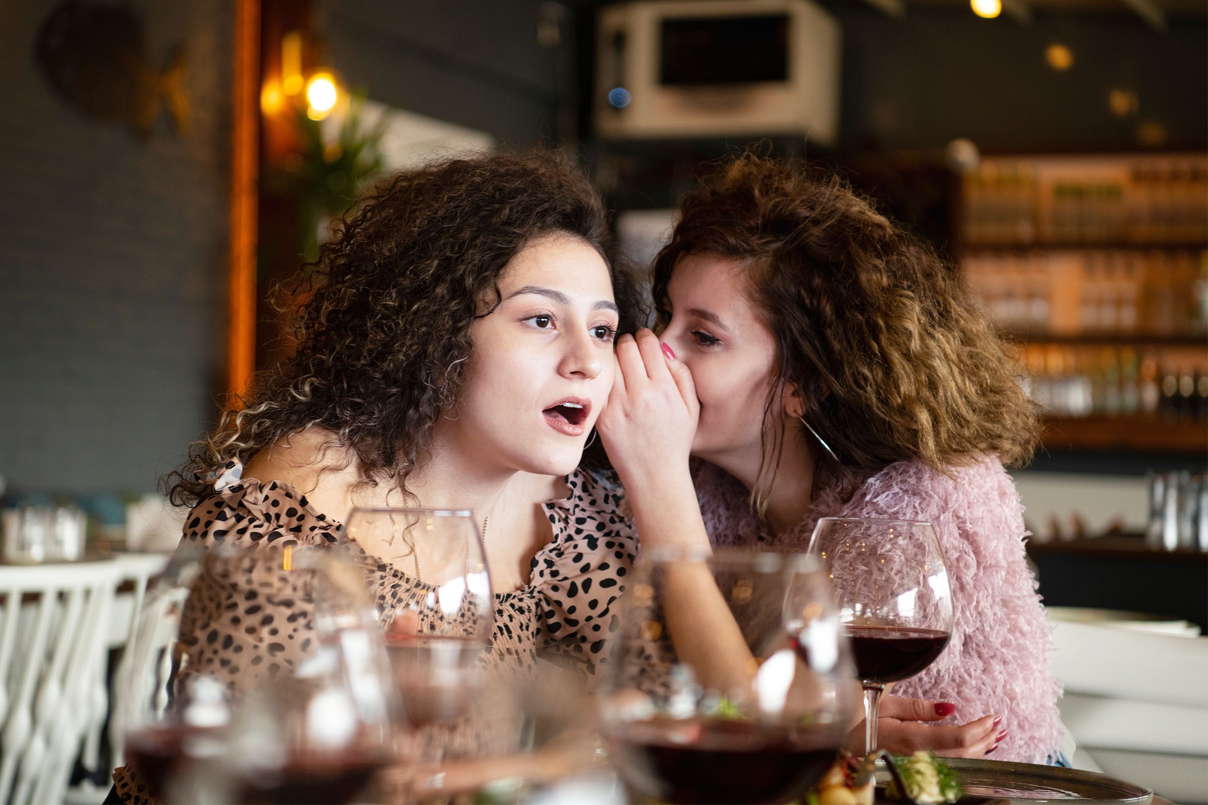 Girls gossiping at a restaurant, shocked face