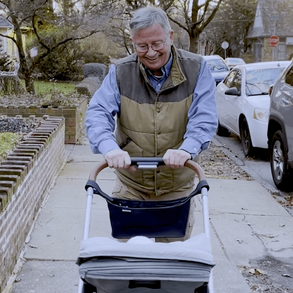 older man smiling, looking down as he walks with stroller