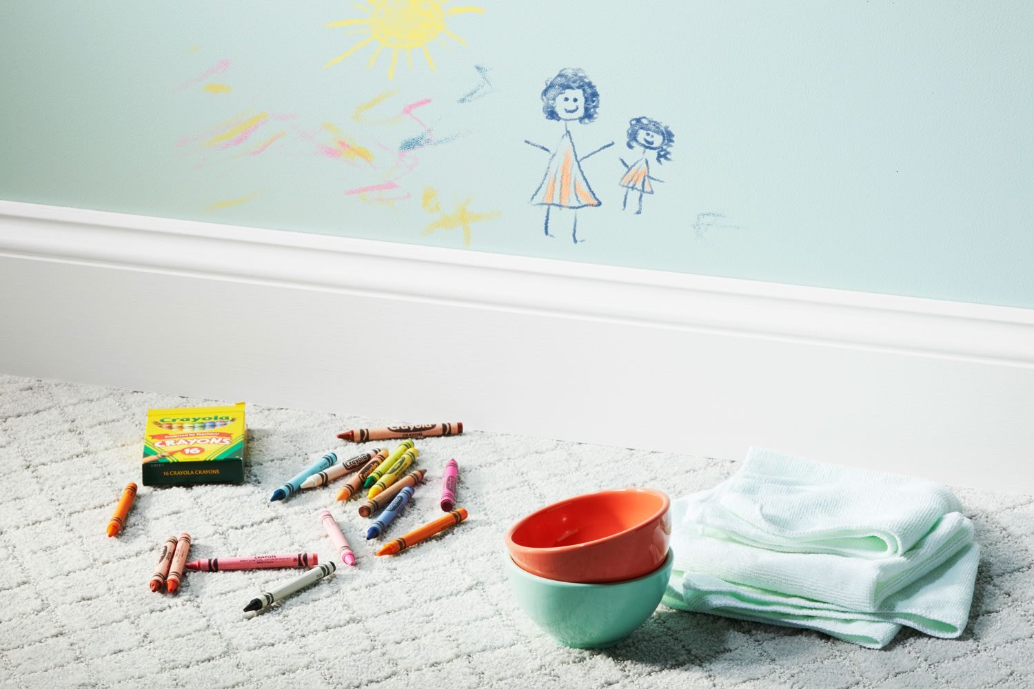 crayon drawing on a light blue wall with crayons, bowls, and cleaning cloths on the floor