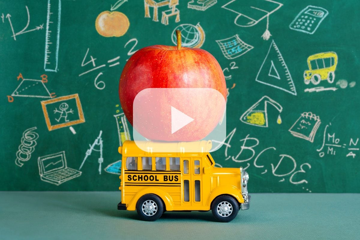 apple on a toy school bus with a chalkboard in the background and a youtube play button overlay in the center