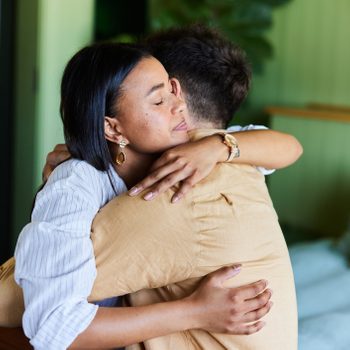 Loving woman hugging her upset husband in their bedroom at home