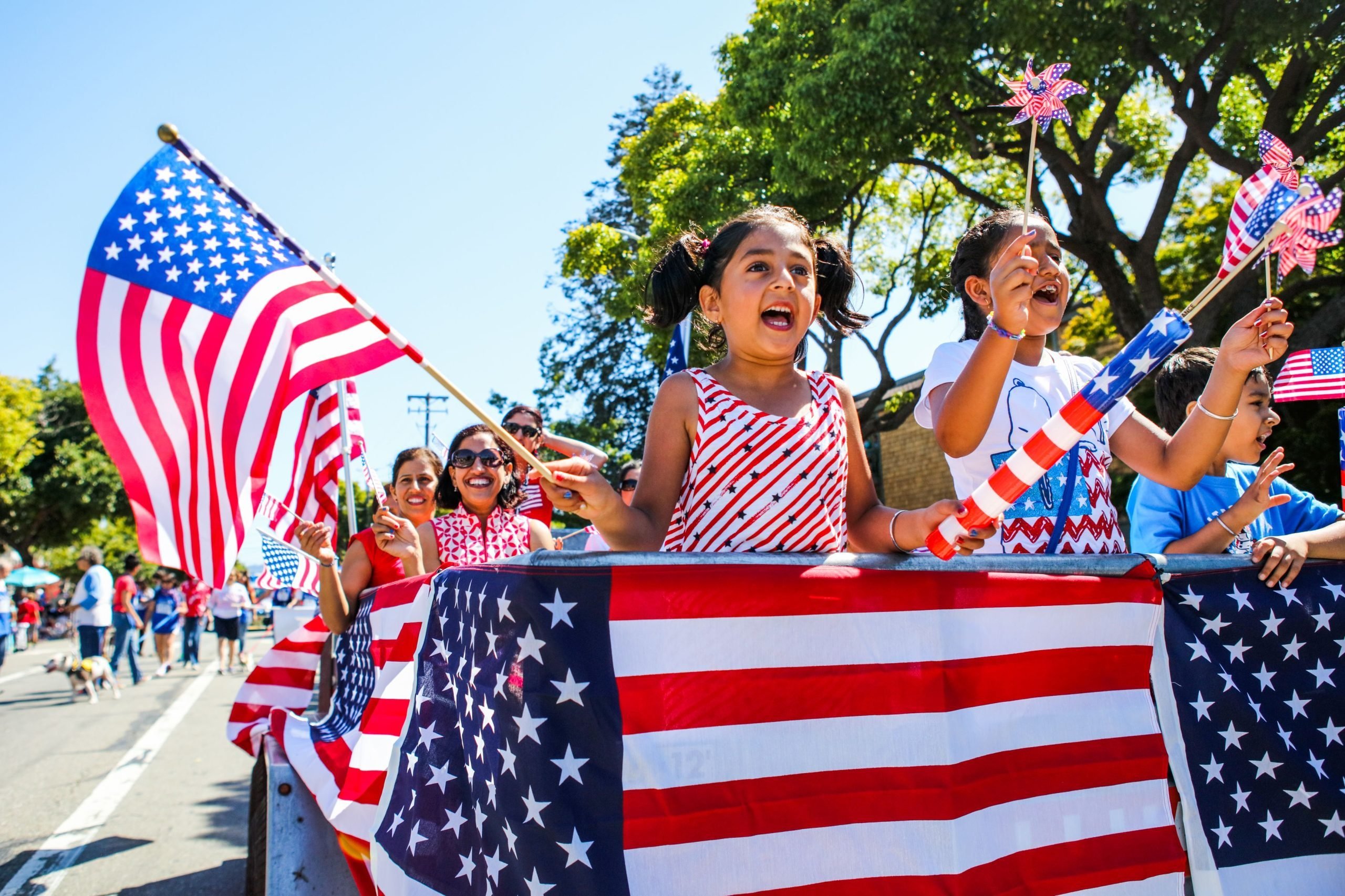 People wave American flags as they ride through 4th of July Parade in Alameda, California on Monday, July 4, 2016.