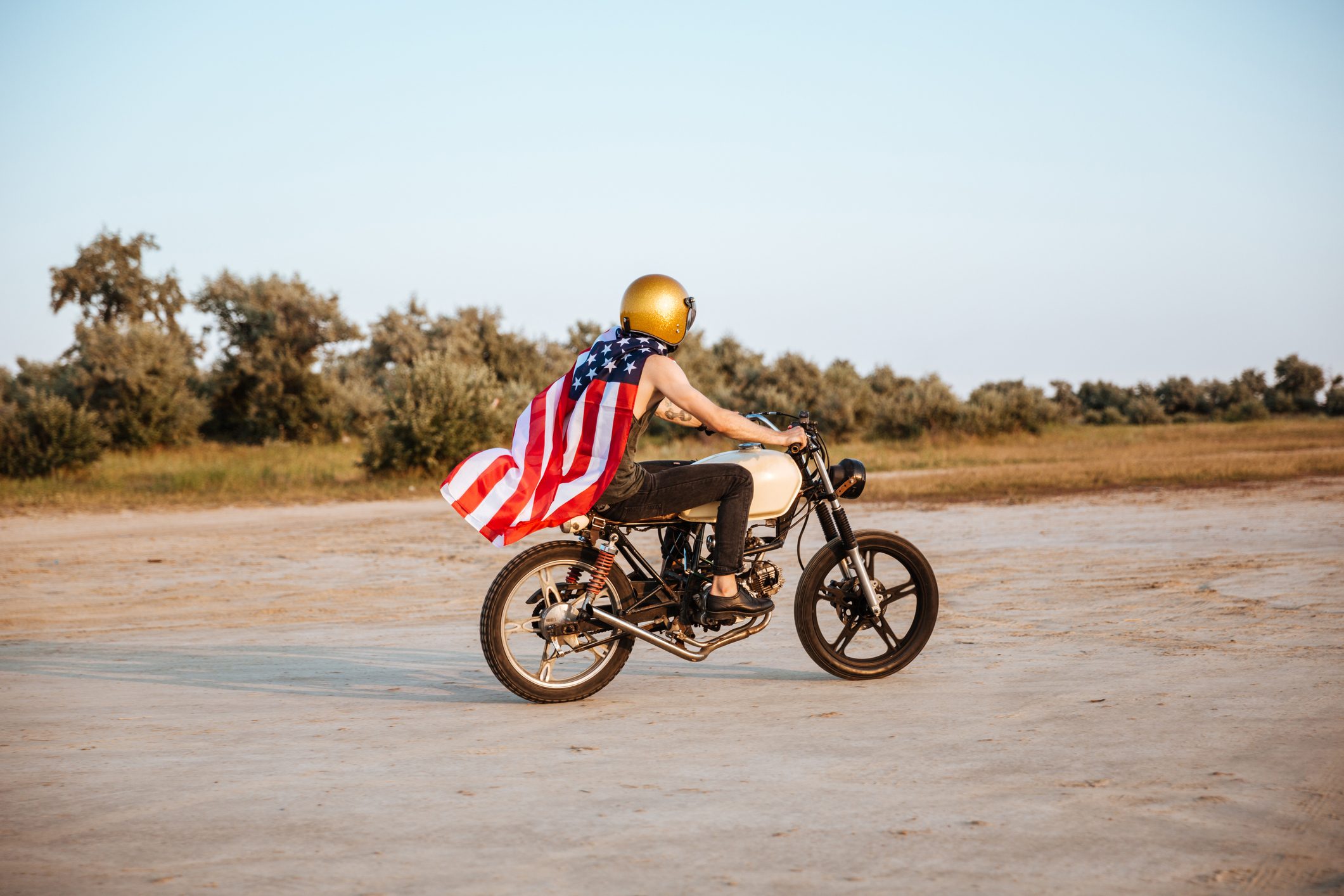Side view of man in american flag cape driving motorcycle