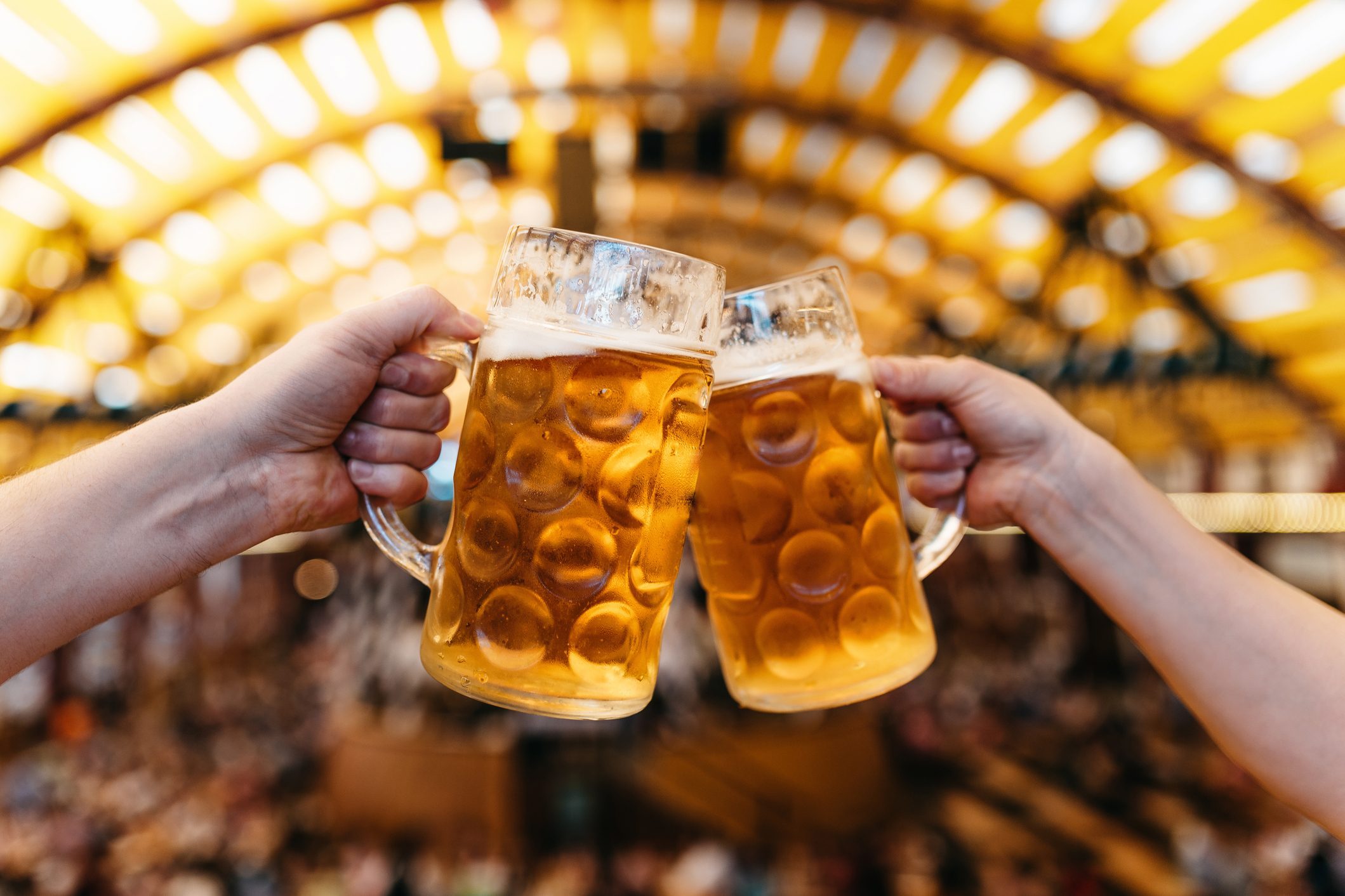 two hands clinking beer glasses in octoberfest marquee