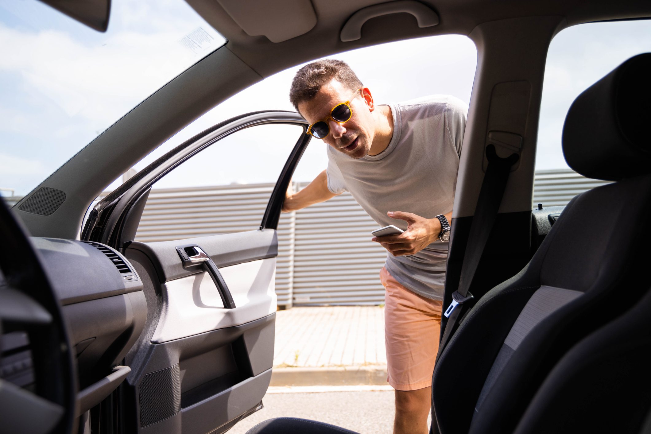 Man holding a smartphone getting into a ride sharing car at the front passenger side door