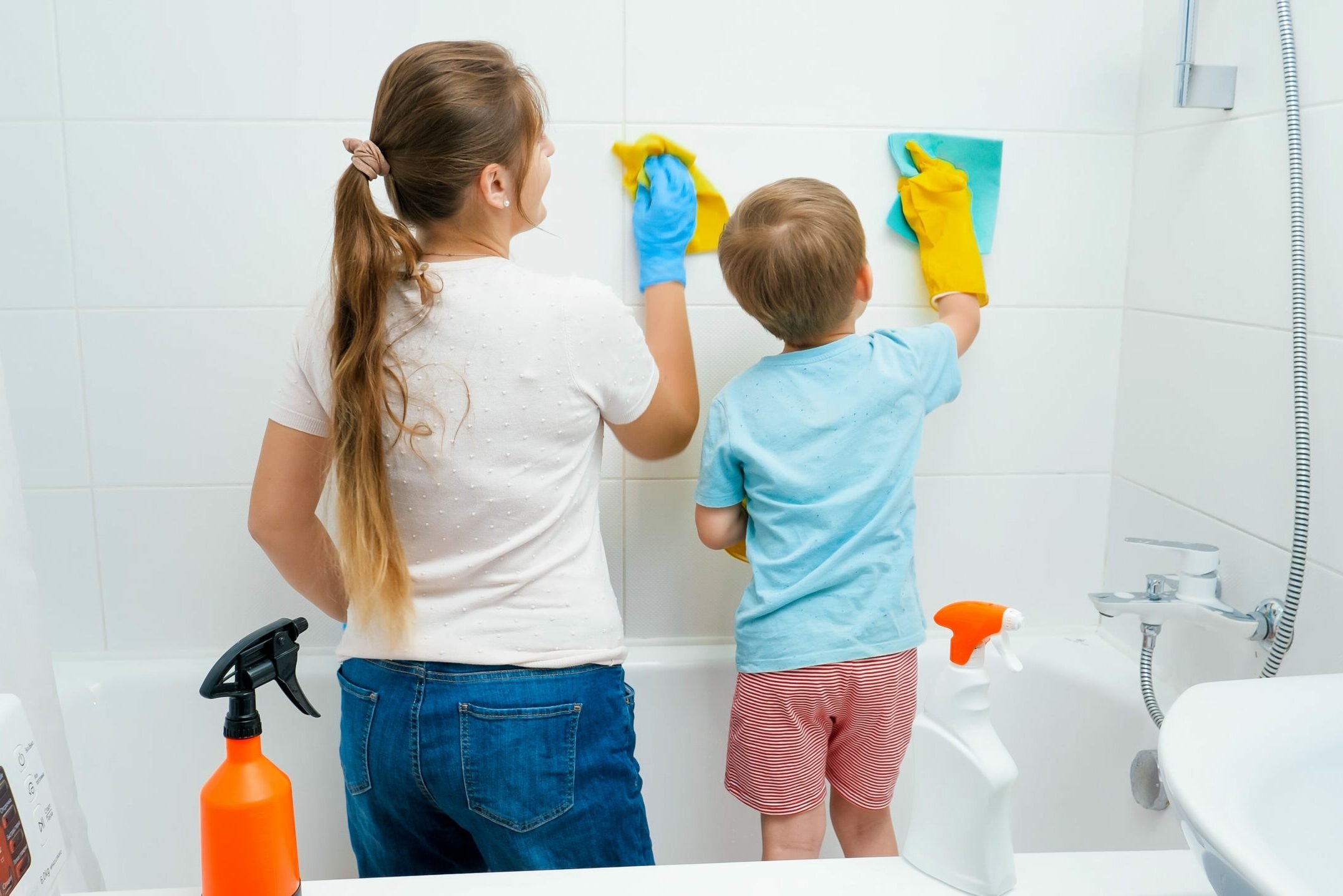 Little toddler boy with young mother washing and cleaning tile walls in bathroom while doing housework and home cleanup